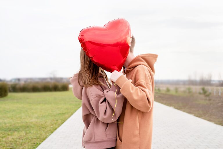 Gutt og jente som kysser bak en rød ballong formet som et hjerte