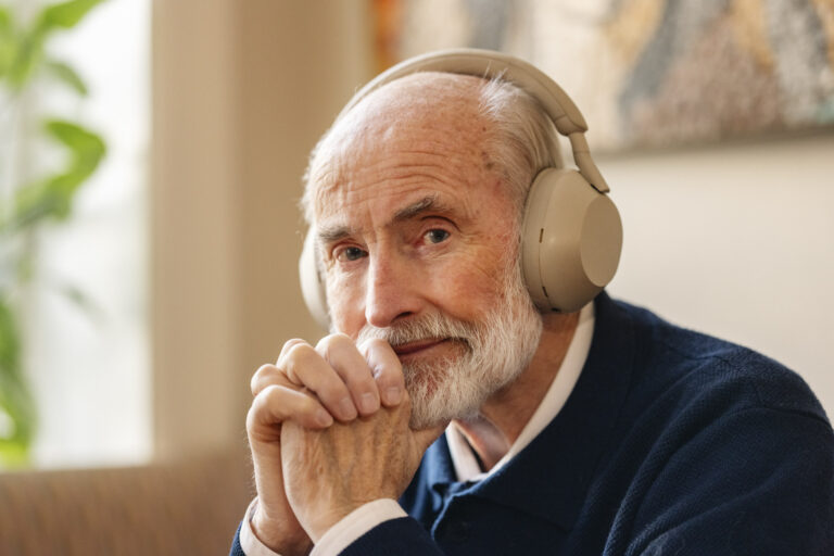 Eldre mann med hodetelefoner, lytter til lydbok og smiler litt.