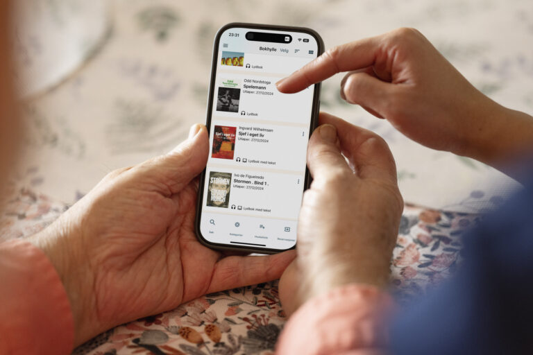 Mobiltelefon med Tibi-appen og eldre hender. En hjelpende hånd peker.